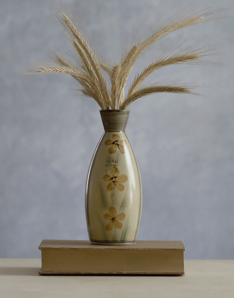 Bundle of rye grass inside a ceramic vase with painted flowers standing on a vintage book